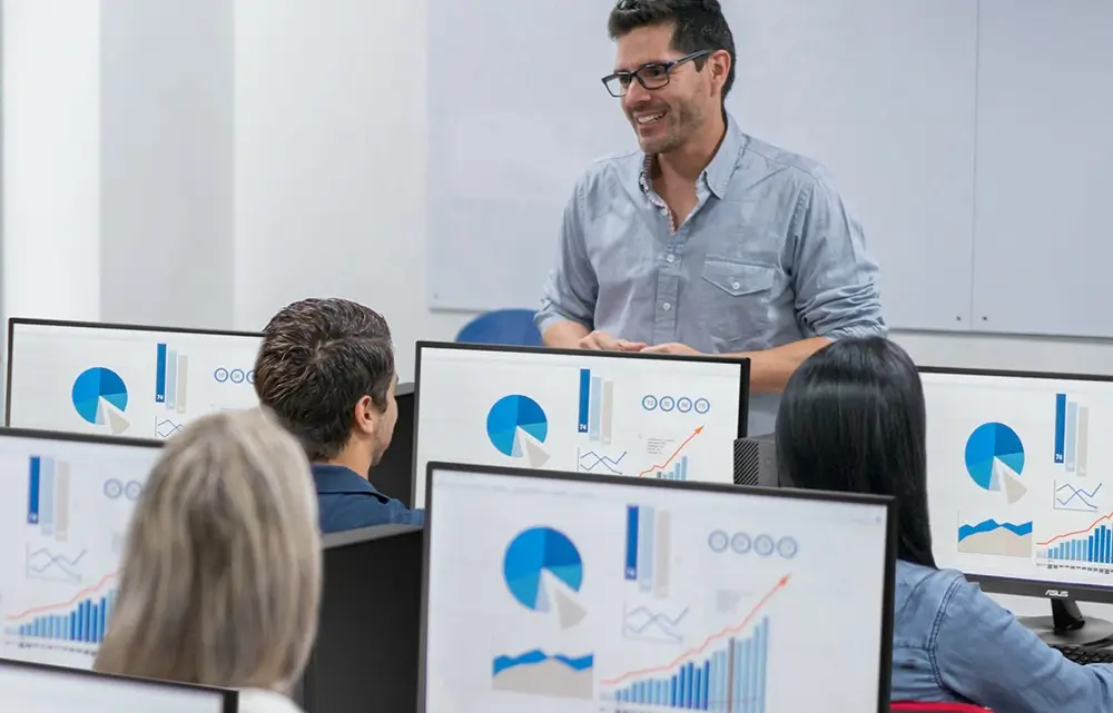 A man standing whilst students work on desktops